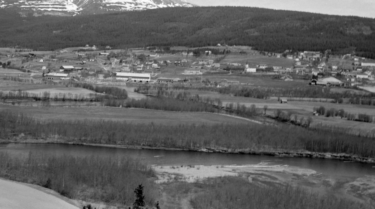 Kommunesenteret i Alvdal i Hedmark, fotografert fra vestsida av dalføret i 1963. I forgrunnen ser vi elva Folla, som på denne elveslette forenes med Glåma. Vi ser Steibrua til venstre i bildet. på østsida av elva her ligger Stei-gardene, med blant annet Storsteien landbruksskole, Litt høyere oppe i lia, til venstre, skimter vi taubanestasjonen, der svovelkisen fra Folldal gruver ble lastet over på jernbane. Til høyre ser vi kirka og kommunesenteret ved jernbanestasjonen.