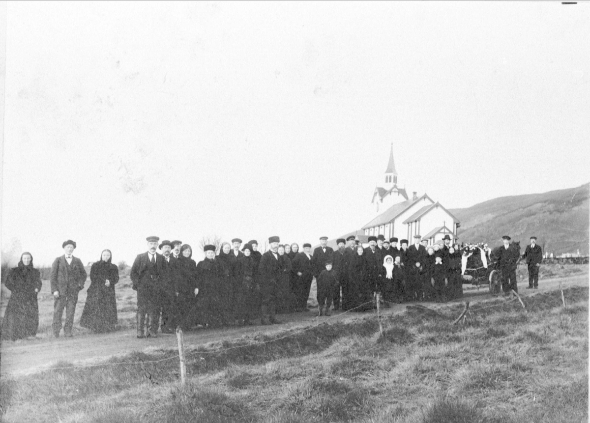 Begravelsesfølge med hest og vogn. Kvæfjord kirke i bakgrunnen.