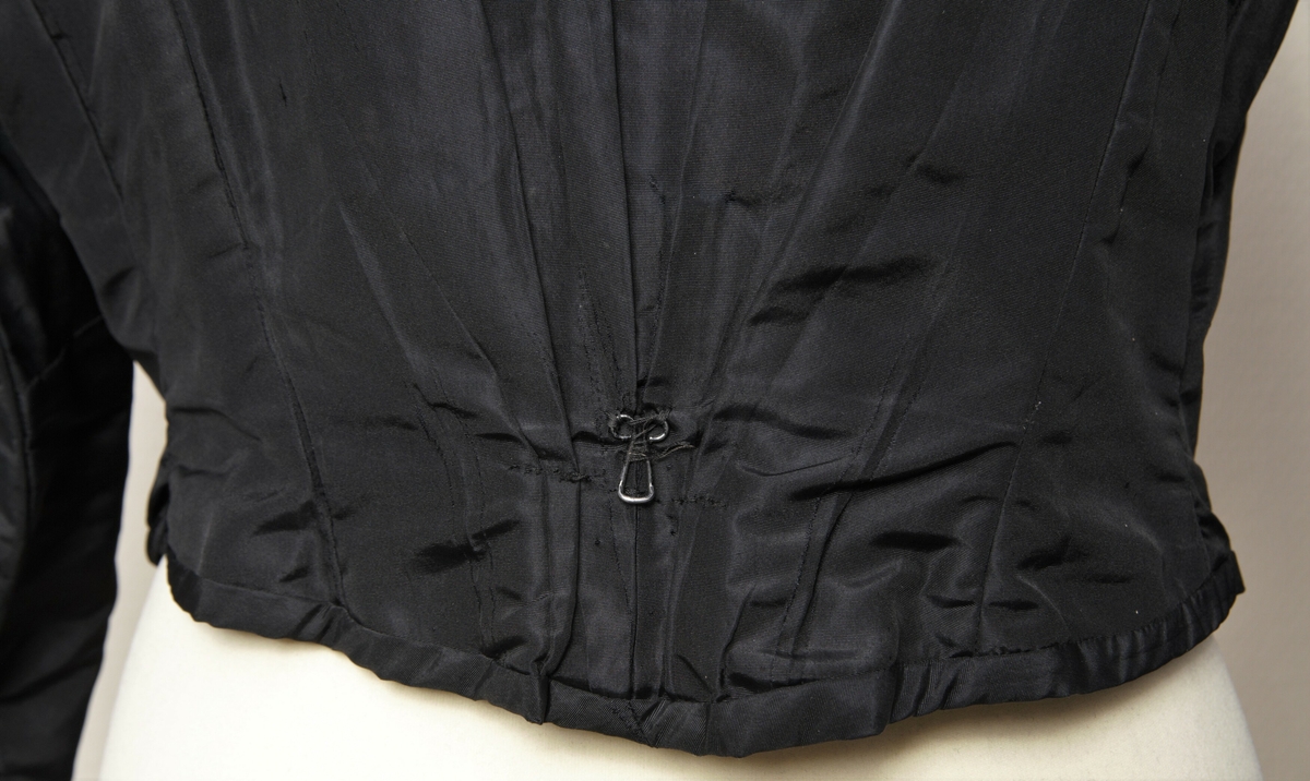 Kvinnetrøye eller kjoleliv sydd i svart silketaft. Med isydde spiler. Dobbel lukking foran. 