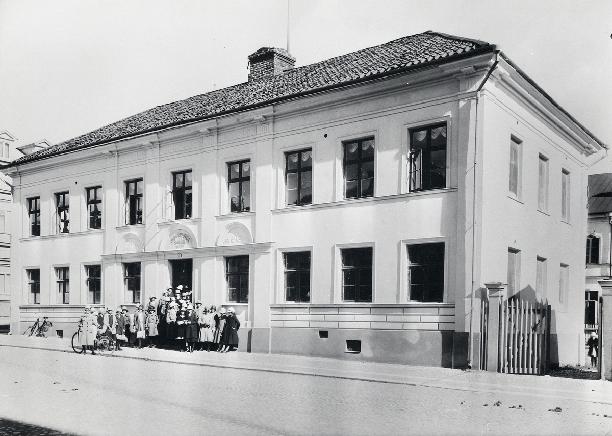 Sjögrenska skolan vid Kungsgatan, Växjö, ca 1925. En skolklass med enbart flickor har samlats vid entrén.
Till vänster skymtar en del av Hypoteksbanken, Kungsgatan 12.