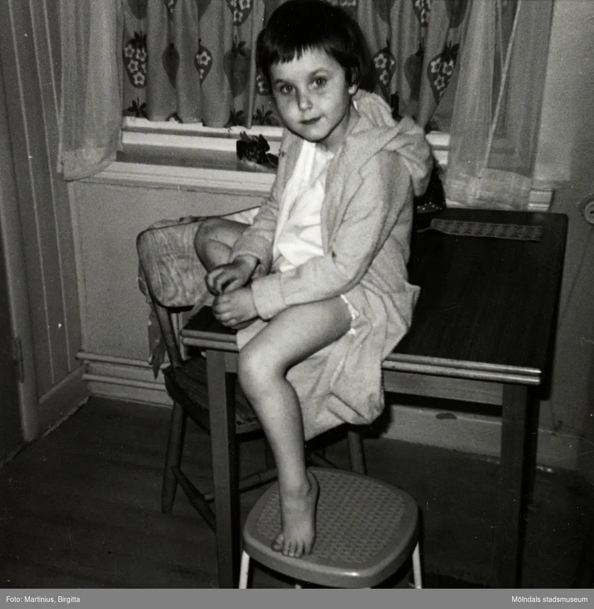 Ilse Tobiasson (född 1960, gift Glimberg), iklädd morgonrock, sitter på köksbordet hemma i familjens lägenhet på Krokslättsgatan 3 i Mölndal år 1964/65.