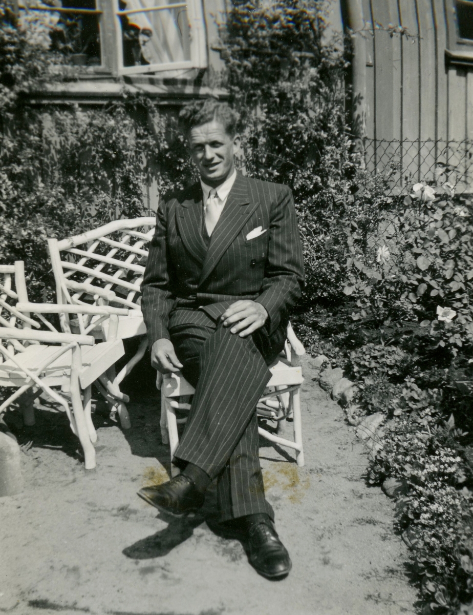 Midsommar 1940. Björn Ekman (1913 - 1992) sitter och poserar i trädgårdsmöblerna utanför sina svärföräldrars hus i Kålltorp. Han gifte sig senare med Mary Ekman och paret bosatte sig i Kållered. Relaterat motiv: A2855.
