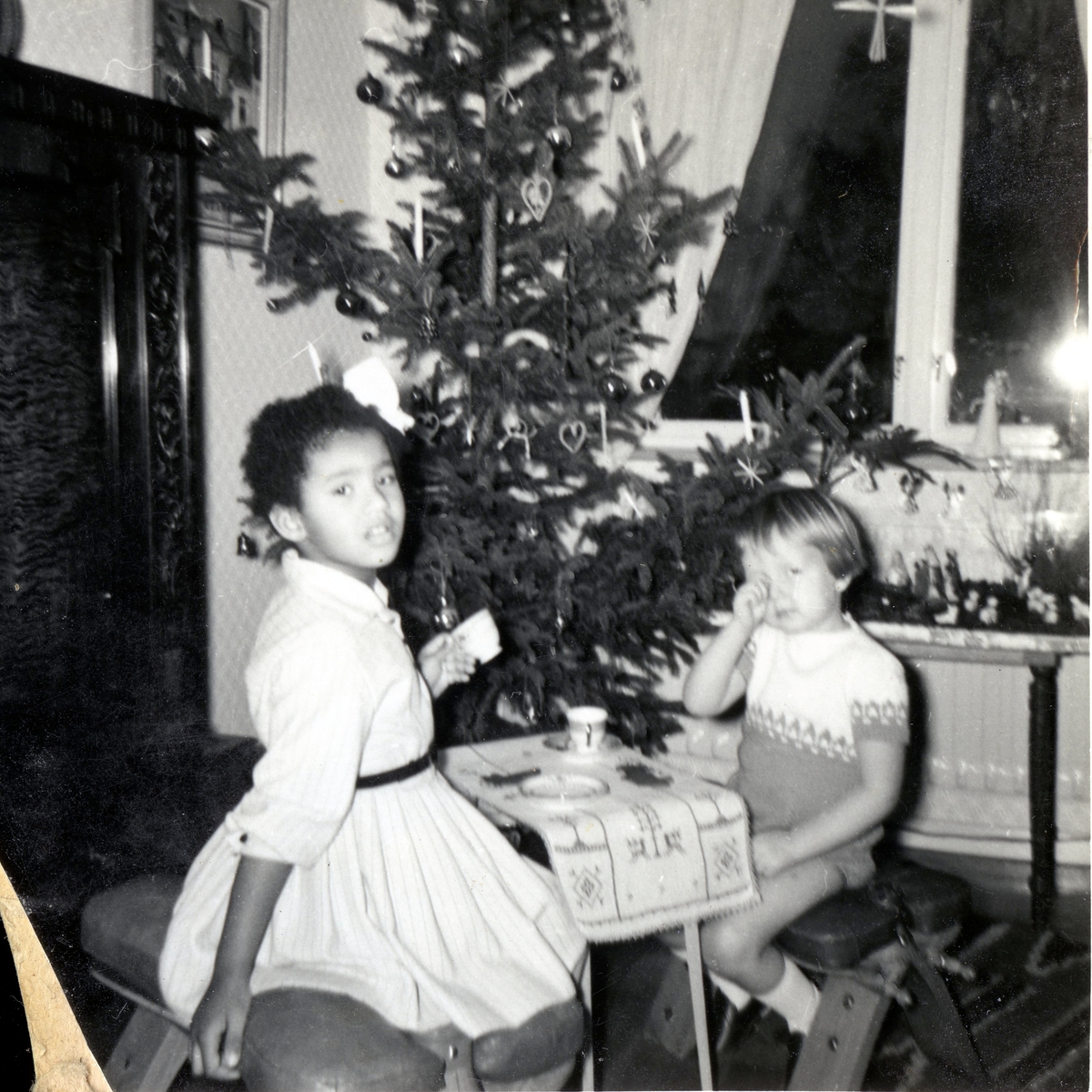 Två små vänner sitter vid ett litet bord framför julgranen och "dricker kaffe" i Manne Ekmans föräldrahem, Rothwalls hus på Streteredsvägen 31 Kållered år 1959. Från vänster: Susanne Kullbring (född 1953) och Manne Ekman (född 1955). Susanne och Manne var barndomskamrater och bodde grannar. Relaterat motiv: A2873.
