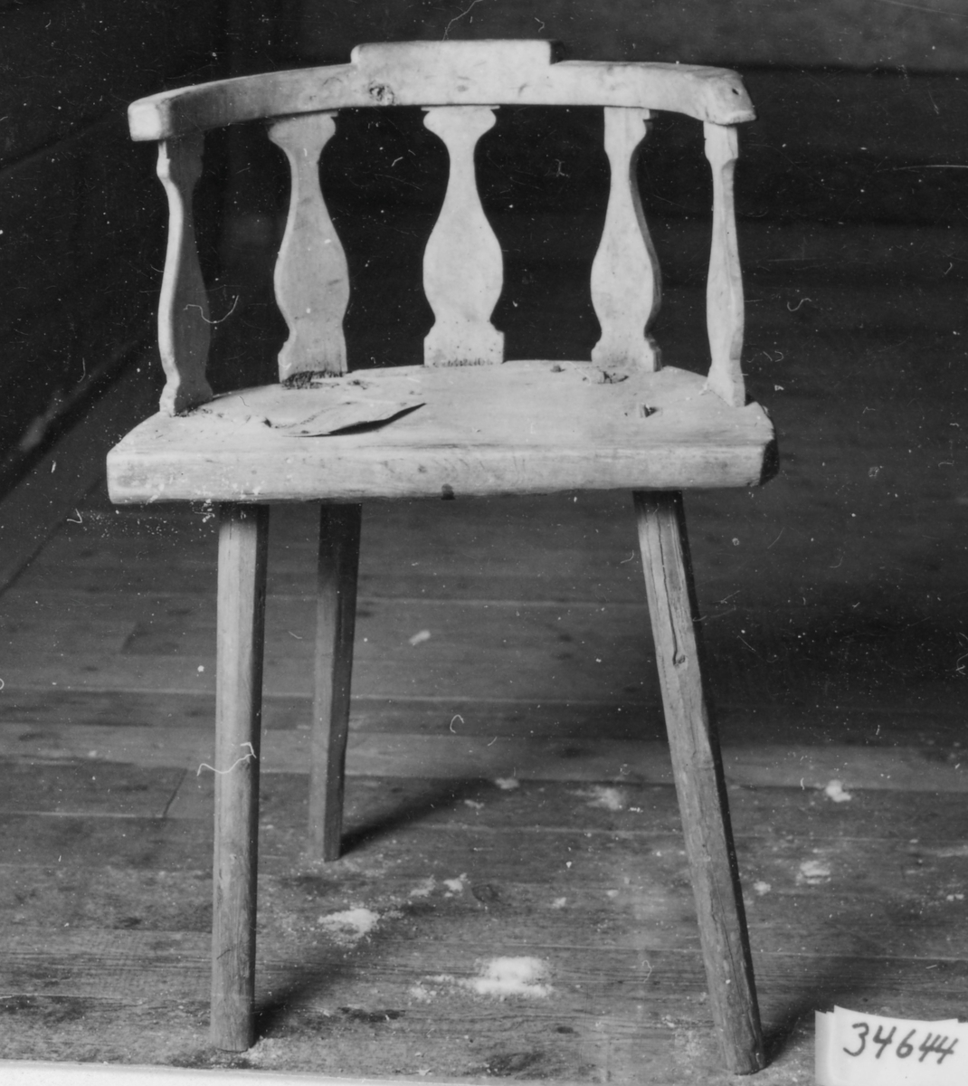 Omålad stol med fyra 8-sidiga intappade ben något utställda. Halvcirkelformad sits, rundad rygg med 5 vertikala balusterformade spjälor sammanfogade med rundat krön, Sitsen förstärkt med påspikat  järnband.