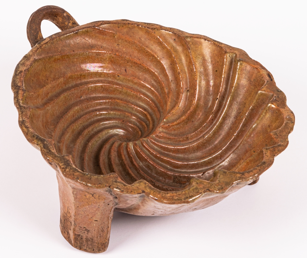 Puddingform, keramik. Snäckformad med våggrepe och tre kraftiga ben.