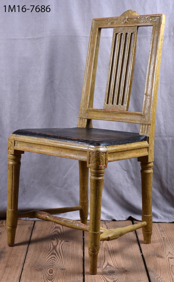 Gråmålad gustaviansk stol med svart sits, svarvade ben med kannelyrer, svarvat benkryss. Genombruten rygg med 4 st spjälor, skuret krön med blomm och bladmönster.