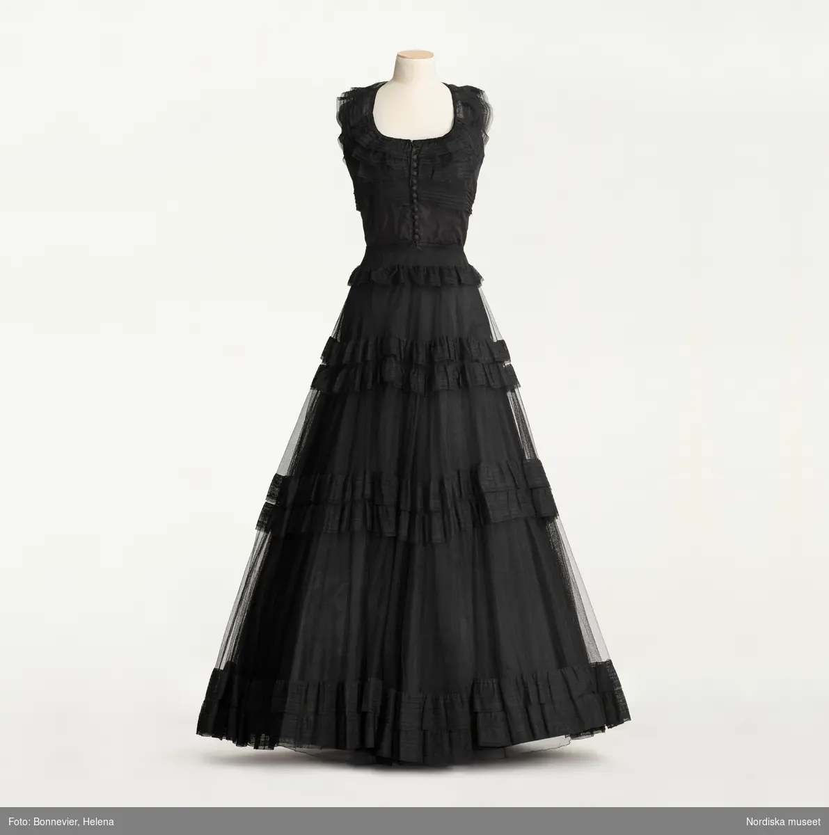 Svart balklänning av siden och tyll, kjolen hålls ut av en styv underkjol. Influerad av Hollywoods kostymfilmer. Beställd från NK:s Franska damskrädderi av Aina Cedervall född Görling (1890-1956). Levererad ca. 1941-1945.