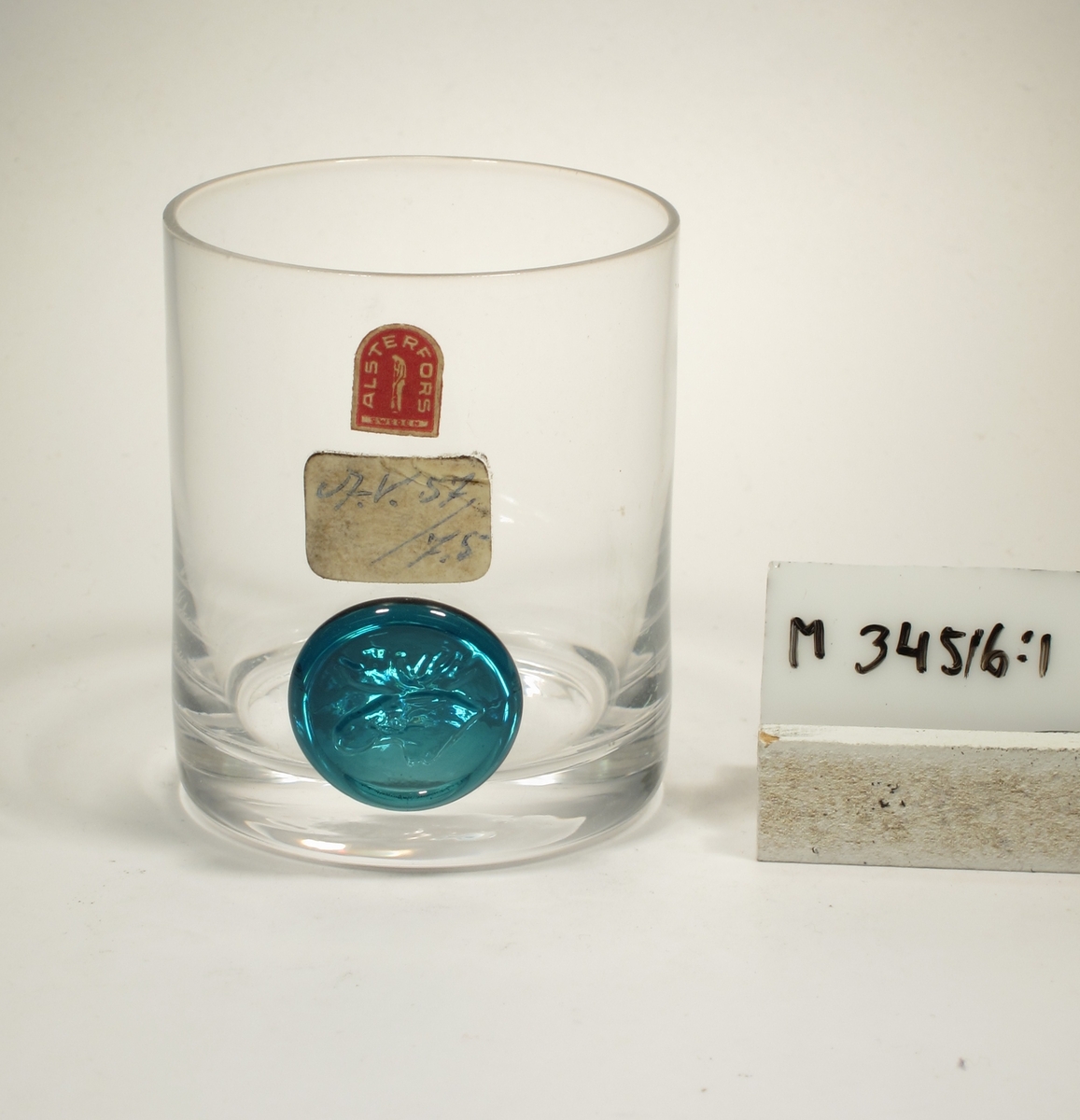 Design: Brukets egen formgivning. Cylinderformad kupa med påklippt blått märke som stämplats med ett älghuvud.
Etikett: Bågformad, röd med vit text, glasblåsare i mitten: ALSTERFORS SWEDEN