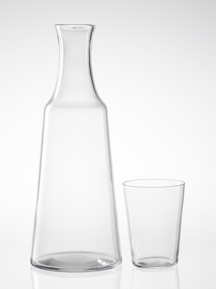 Formgivare: Edvin Öhrström. Vattenkaraff med tillhörande glas. Karaff med svagt konkav hals och konande buk. Vattenglas vilar upp- och nervänt på karaffens axelparti.