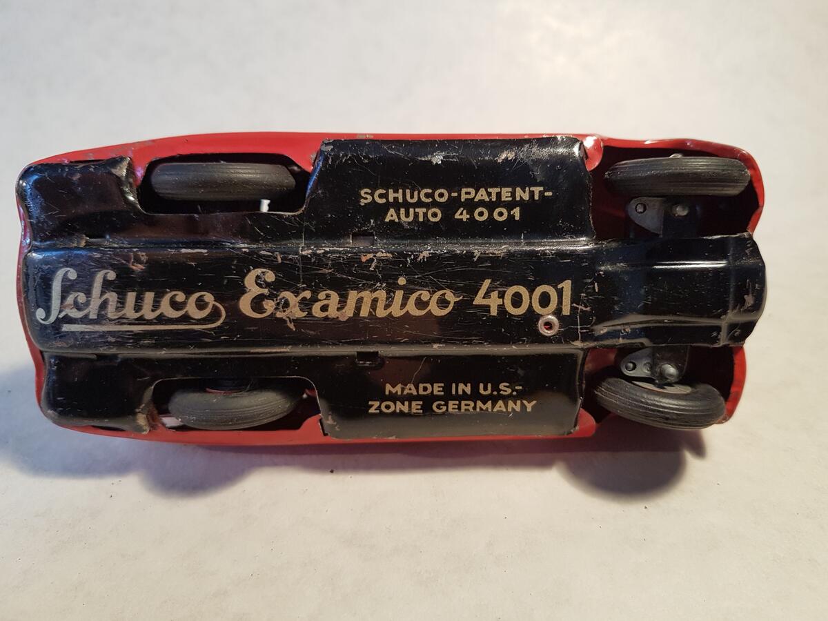 En röd leksaksbil för två personer. Den kommer från leksaksföretaget Schuco. Modell Examico 4001. Tillverkad i: US-Zone Germany. Tidigare uppdragbar, nyckel saknas. Vindruta saknas.