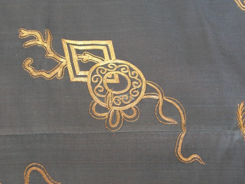 Kvnnojacka, troligen använd av mandarinhustru, en ämbetsdräkt. Bärs vanligen tillsammans med byxor eller veckad kjol.
Blåsvart sidentyg, tuskaft. Rak ärm.
Fram- och bakstycke dekorerade med guldbroderi, läggsöm sydd med tvärstygn, roströd silketråd. Guldtråden är gjord av pappersguld virad runt en silkekärna. Vissa mönsterformer har en klassisk symbolik, t.ex. ärtskidan för fruktbarhet, andra former är av mer dekorativ art.
Dekorativa band runt framkant, nederkant och sprund. Ytterst ett kantband i blått siden, därefter ett band, silkebroderi, 3,5 cm,  blommor och cirklar i vitt och olika blå nyanser samt guldbroderi, innerst ett mönstervävt band, 2 cm brett. I halsringningen ytterst ett kantband i blått siden, därefter ett band, silkebroderi, likadant som på kantningen runt nederkanten, därefter en snedremsa i siden , ca. 1 cm bred, och innerst ett mönstervävt bant, 1.5 cm brett.
På ärmen snedremsa i blått siden, ca. 1,5 cm bred därefter band i silkebroderi likadant som runt nederkant och halsringning. Ytterst ett tyg, 12 cm brett, dekorerat med mönstervävt band i blått och guldfärg. Tyget är broderat? med tråd i liknande färg som tuskaftsbottnen. Åtdragen plattsöm som bildar mönster tillsammans med den något grövre tråden. Symboliska mönsterformer, de 8 taoistiska symbolerna,  bl.a. flöjt, solfjäder och lotusblomma mellan dessa dekorativa mönster, S-formade. Ärmens baksida och ca. 1/4 av framsidan täckt med guldbroderi, läggsöm sydd med tvärstygn, guldfärgad tråd, och detaljer i silkebroderi, svart, vitt och lila, platt- knut och klyvsöm. Mönstret föreställer bl.a. vattenströmmar, vågskvalp och en drake som stiger upp ur vattnet. Draken har 4 klor och symboliserar den näst högsta rangen, den högsta har 5 klor och det är kejsarens symbol. Draken är en positivt laddad symbol, en manlig symbol.
Jackan knäpps med tre klotformade mässingknappar och öglor gjorda av svarta, runda band.
Foder: ljusblått siden.
En märkning på  höger framstyckes insida i halsringen, kinesiska tecken skrivet på tyget och på en vit klisterlapp.
Uppgifter om detta plagg, dess  historia och symbolik är inhämtade från Marianne Erikson, tidgare intendent vid Röhsska museet.

Funktion: Kina,