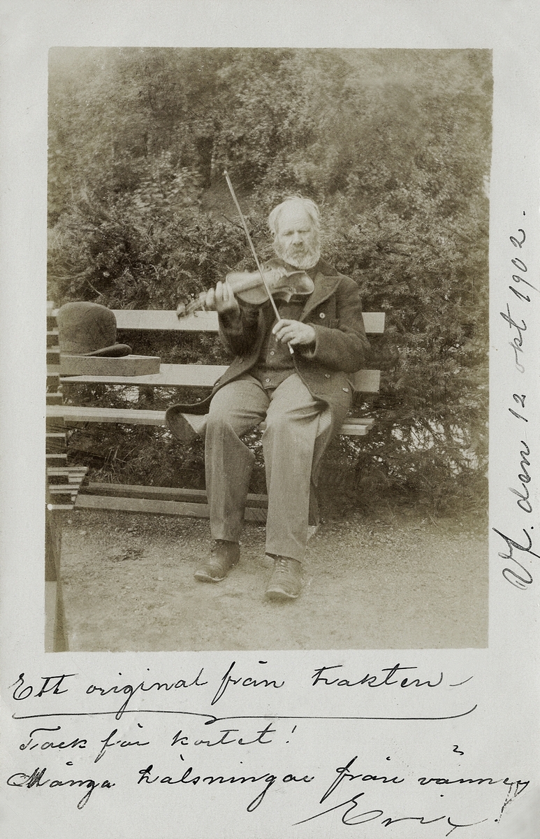 Foto av en äldre man som sitter på en trädgårdssoffa och spelar fiol.