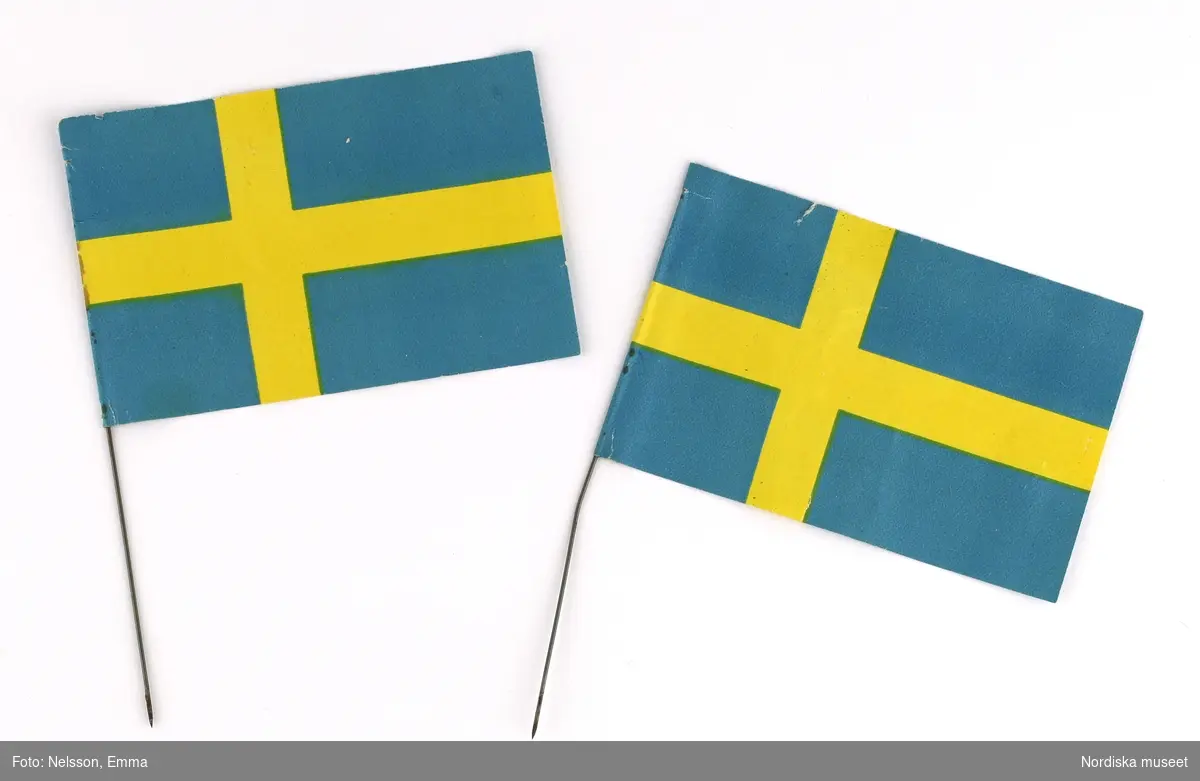 Fyra stycken (a-d) julgransflaggor föreställande den blå-gula svenska flaggan. Två stycken var placerade på var sida om julgranens topp. Av papper med metallstång som fastsättningsanordning.

Lena Kättström Höök 2019-03-21