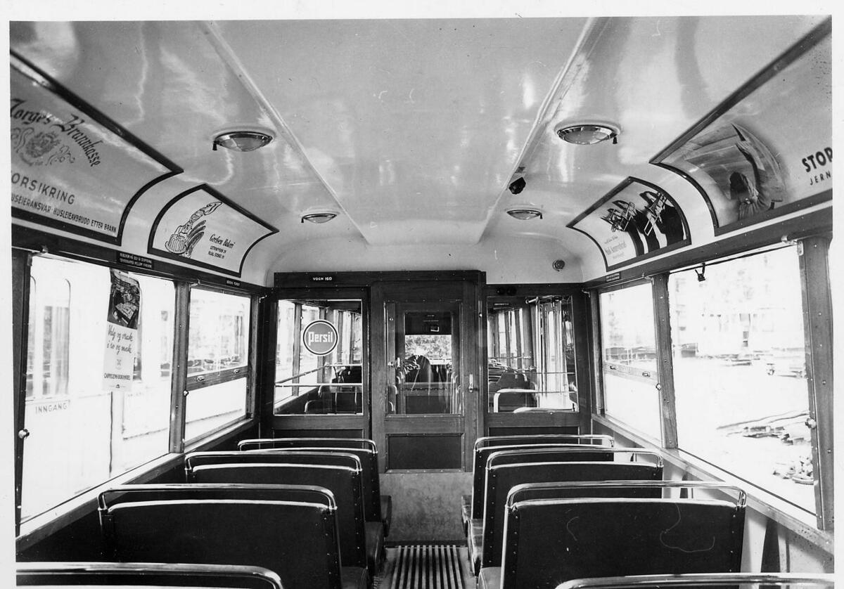 Interiør i vogn nr. 160. Interiøret består av doble seter på hver side, store vinduer med trelister og lyst tak med reklame fra blant annet Grefsen Bakeri og forsikring fra Norges Brannkasse.