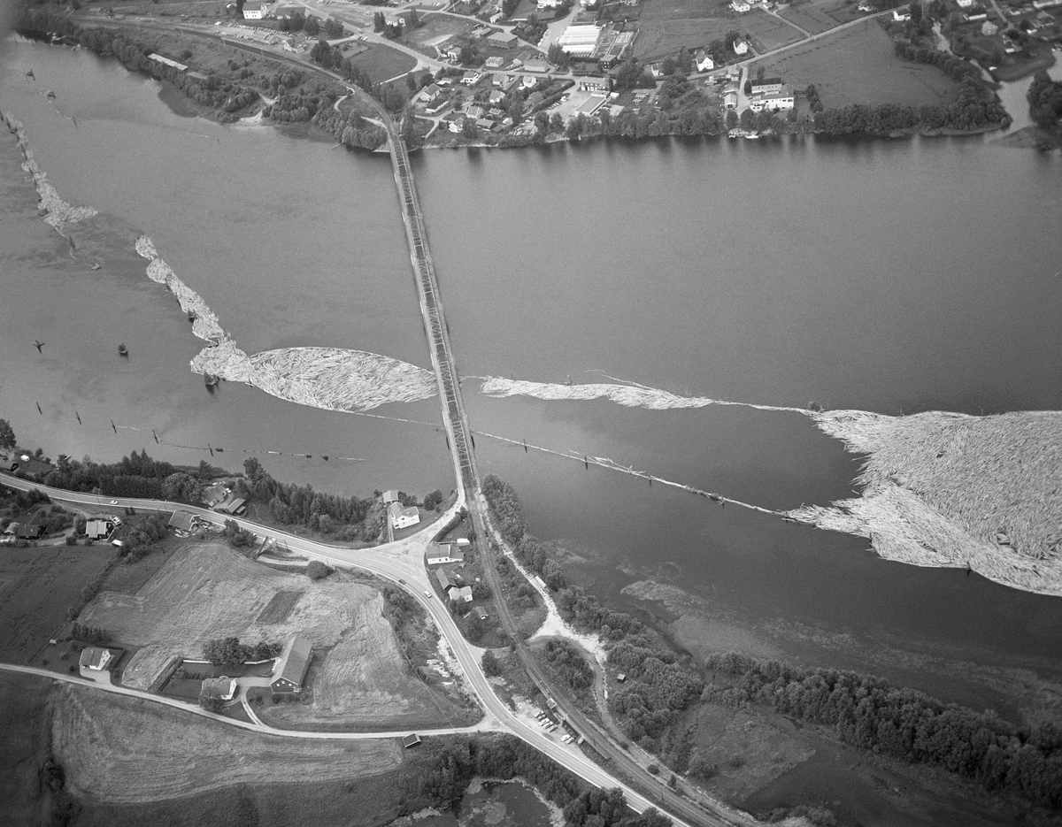 Flyfotografi, tatt over Fetsund lenser i Fet kommune i 1985, som var det siste året med tømmerføting i Glomma. Vi ser ned mot det stilleflytende vannspeilet, der det stakk opp «gæljer» (pålekonstruksjoner) som var rammet ned i elvebotnen som støttepunkter for de flytende lensestokkene. Da dette fotografiet ble tatt var det bare lenseinnretningene langs den vestre elvebredden som var i bruk. I den nederste delen av dette anlegget ble tømmerstokkene «moset» for buksering over den nedenforliggende innsjøen Øyeren med slepebåt. Tømmeret ble sluppet porsjonsvis ned mot Fetsund fra attholdslensa ved Bingen, cirka åtte kilometer lengre nord. 1985 var det siste året det ble fløtet tømmer i Glomma, og dette året var det bare hovedvassdraget fra Rena i Åmot og sørover som hadde fløting. Fløtingskvantumet hadde et volum på 126 014 kubikkmeter, som var et svært beskjedent tall sammenliknet med hva som var vanlig i dette vassdraget en generasjon eller to tidligere. Siden 1978 hadde det bare vært Borregaard fabrikker i Sarpsborg som hadde kjøpt fløtingsvirke i Glommavassdraget, og følgelig var det heller ikke lenger nødvendig med sortering av virket etter påslåtte merker på stokkene.