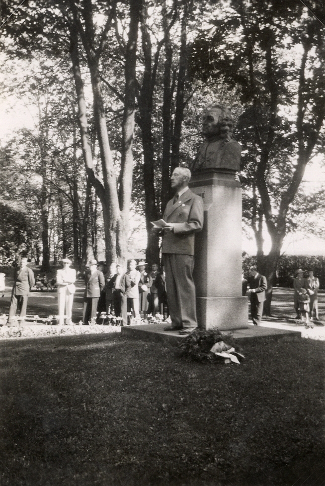 En man i kostym (P G Vejde?) håller tal vid Carl von Linnés byst i Linnéparken, trol. 1947. I bakgrunden syns en handfull åskådare.