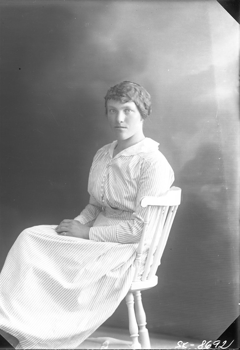 Porträtt av en ung kvinna i randig klänning som sitter på en pinnstol.