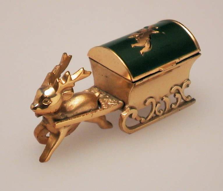 Gullfarget smykkeskrin formet som kiste på slede, dratt av rådyr. Kistens lokk er grønt, og har gullfarket amorfigur. Kisten er foret med rød fløyel.