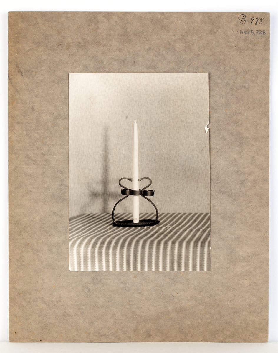 Ett svartvitt fotografi klistrat på två 22 x 28 cm stort grått kartongblad. Fotografiet föreställer en järnljusstake och högst upp på kartongbladet högra hörn finns märkningen "B-978".