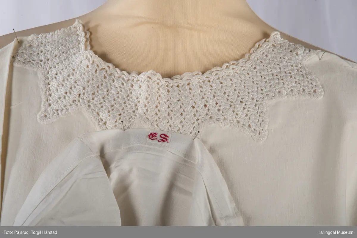 Hvit serk eller nattkjole i bomullsstoff med heklete kanter på hals om rundt ermene.
