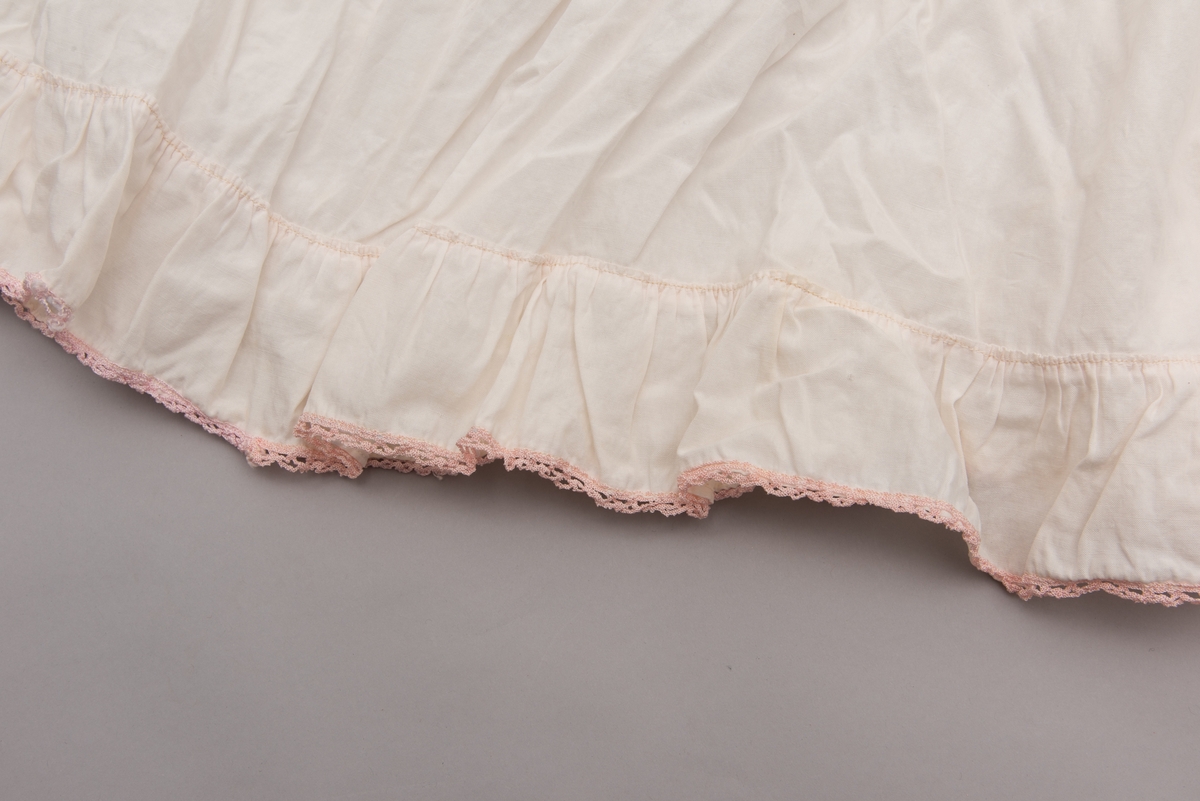 Hvitt formsydd laken med kapper til babykurv. Rosa frotté-innlegg og rosa blonde nederst på kappen.