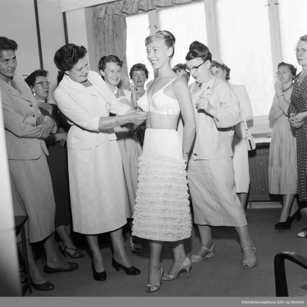 Korsett-eksperten miss Greaway, generalsekretær i Corset Guild of Great Britain, på besøk i Oslo. Til høyre, konsulent fru Irene Priestley-Røstad. Irene Nevermann sto modell. Juli 1957.