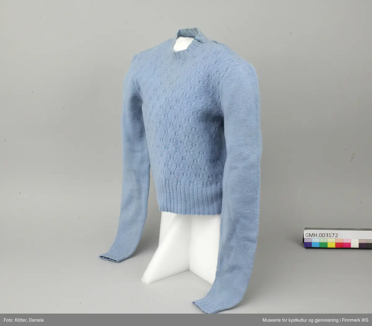 Bare genseren tilsvarer ca. størrelse 6 år. Den er stikket av blå ull. Det er satt inn en glidelås på venstre skulder. For- og bakside av bollen er strikket separat og satt sammen. Forsida har et mønster, mens baksida og armene er glattstrikket.