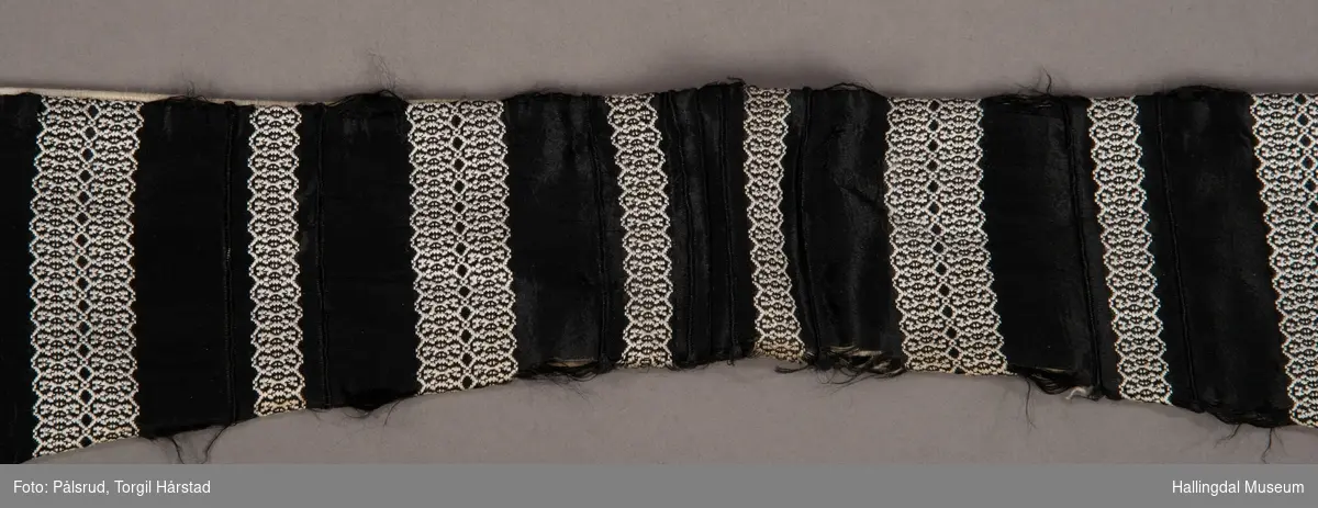 En løsthengende krage i silke/bomull med stripet mønster i hvitt på sort bunn - border. Hvit fôr. Slitte ender.