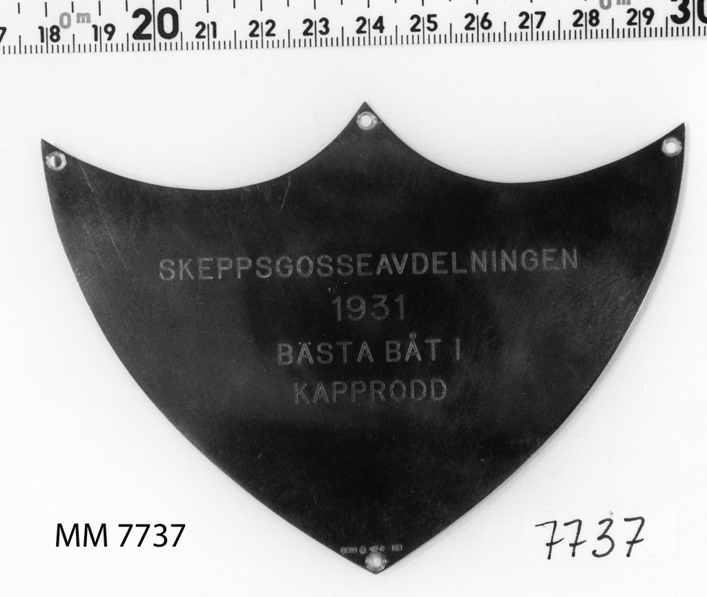 Plakett av silver utan platta.
Inskription: Skeppsgosseavdelningen 1931
Bästa Båt i Kapprodd.