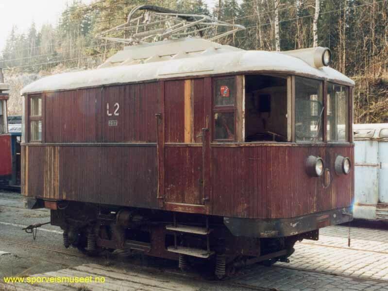 Lokomotiv med eksteriør i tre. Vognen er i en burgunderrød farge med vinduer i front og bak og vognnummer plassert på siden. 