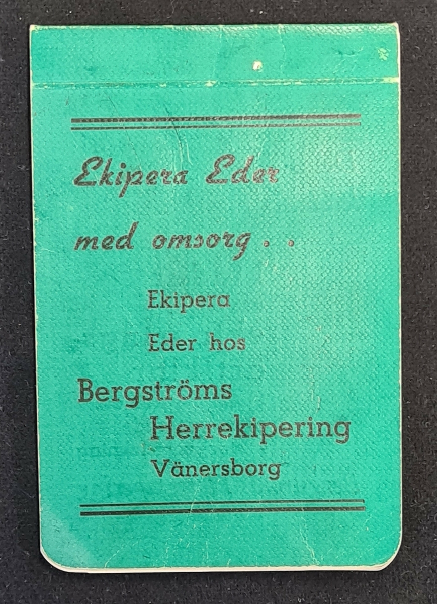 Litet anteckningsblock med grön oärm. På blocket står Ekipera Eder med omsorg...Ekipera Eder hos Bergströms Herrekipering Vänersborg.