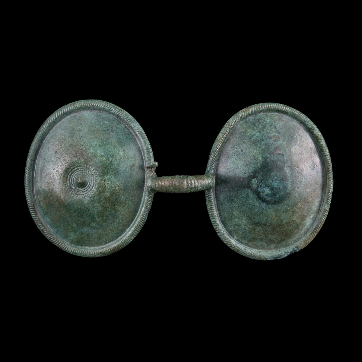 Glasögonformigt spänne, från bronsåldern, omkr. 1000 f.Kr., av brons. L. 14 cm, skivorna äro ovala. Diam. 7 x 6 cm, lätt kupiga, längs kanten löper spiralläggningen som en bård. Bygeln mellan skivorna likaså refflad. Ena skivan har en uppstående mittknopp och runt denna koncentriska cirklar och en uddkant ytterst. Andra skivans mitt pryds av nålens bricka, ornerad med punkter och streck. Nålen avbruten. L. 4,9 cm. Under bygeln en treflikig förstärkning, vid fästet på skivorna. Nålens platta oval, diam. 1,7 x 2 cm. Se tidn. art. VA 2 maj 1960, 3 maj 1960. Upphittat av fru Tyra Tjernberg, 1 maj 1960, ca 150 m. S. om mangårdsbyggnaden, Sebäng 5:1. Spännet låg i skogsmark, moränkulle, alldels invid ägoväg i ett tillfälligt litet grustag, som tagits upp i höstas för att laga vägen. Spännet hade nu glidit ner och låg nu en bit ner i grustaget strax i närheten av ett ca 1,3 m. stort stenblock. Inköpt för 100:- 1960. Alfons Tjernberg, hem.äg., Sebäng, Salsåker, Nordingrå. Tel. 126. 