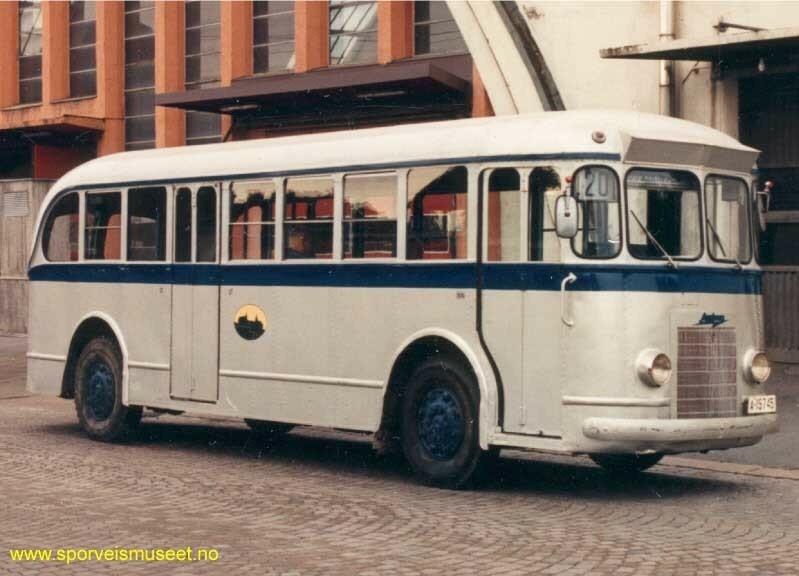 Buss i sølvgrå farge med et mørkt blått bånd som går langs bussen på midten. 