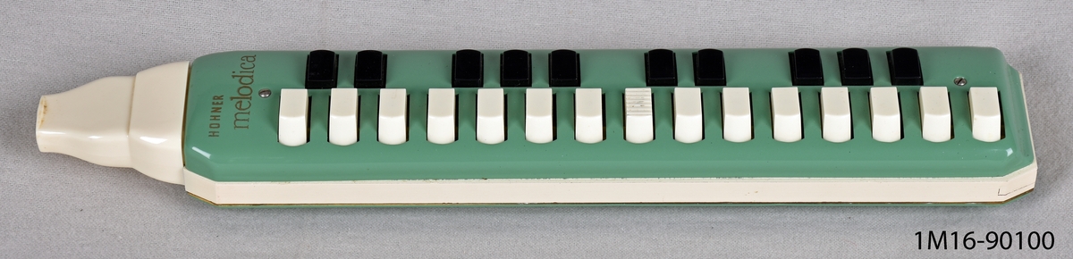 Melodika, i grön och vit celluloid med tangenter i vitt och svart. Märke: Hohner. Vitt och orange fodral med texten: "melodica".