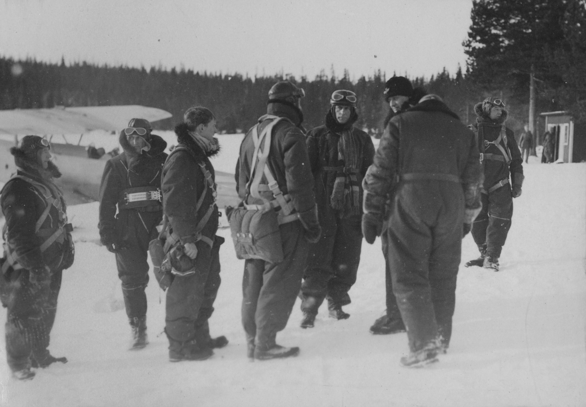 Åtta militära flygare samlade vid flygplan, vintertid, 1930-tal.

Text vid foto: "'Vid flygstn"