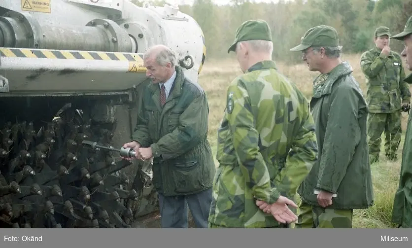 Försöksvagn (stridsvagn 103) med ”minröjningsaggregat Gluff-Gluff”.

På bilden är försöksledare från FMV, C FarbC överste Björn Svensson, Hans Majestät Konungen Carl XVI Gustaf, löjtnant Leif Wisén, och general Curt Sjöö.