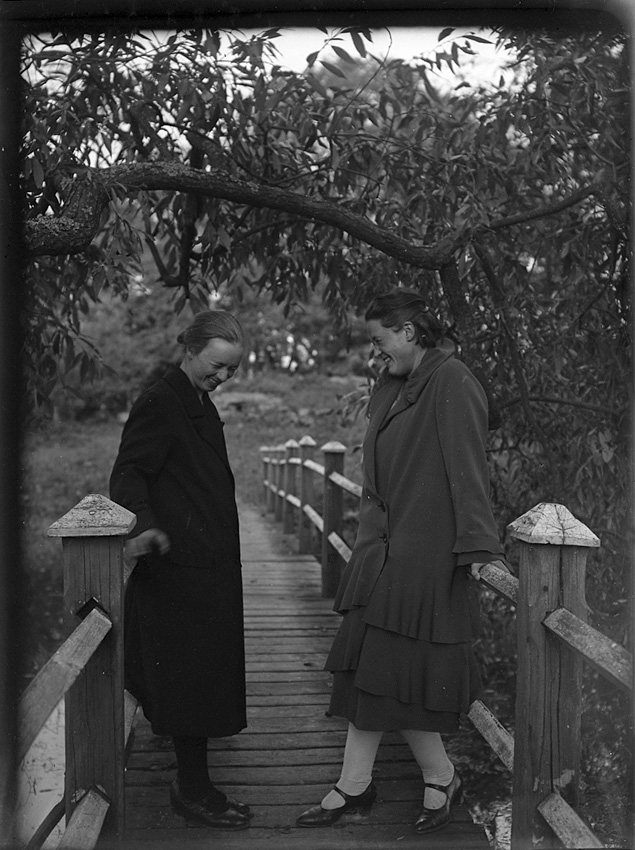Två kvinnor, stående på gångbro i park. Västerås.