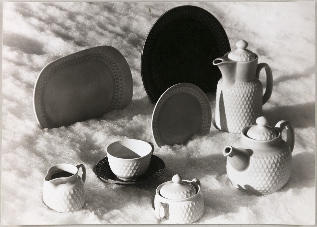 Servise på modell "Triangel" fra Stavangerflint A/S. Avbildet sortiment viser fat, tallerken, kopp med underskål, te- og kaffekanne, fløtemugge og sukkerskål.