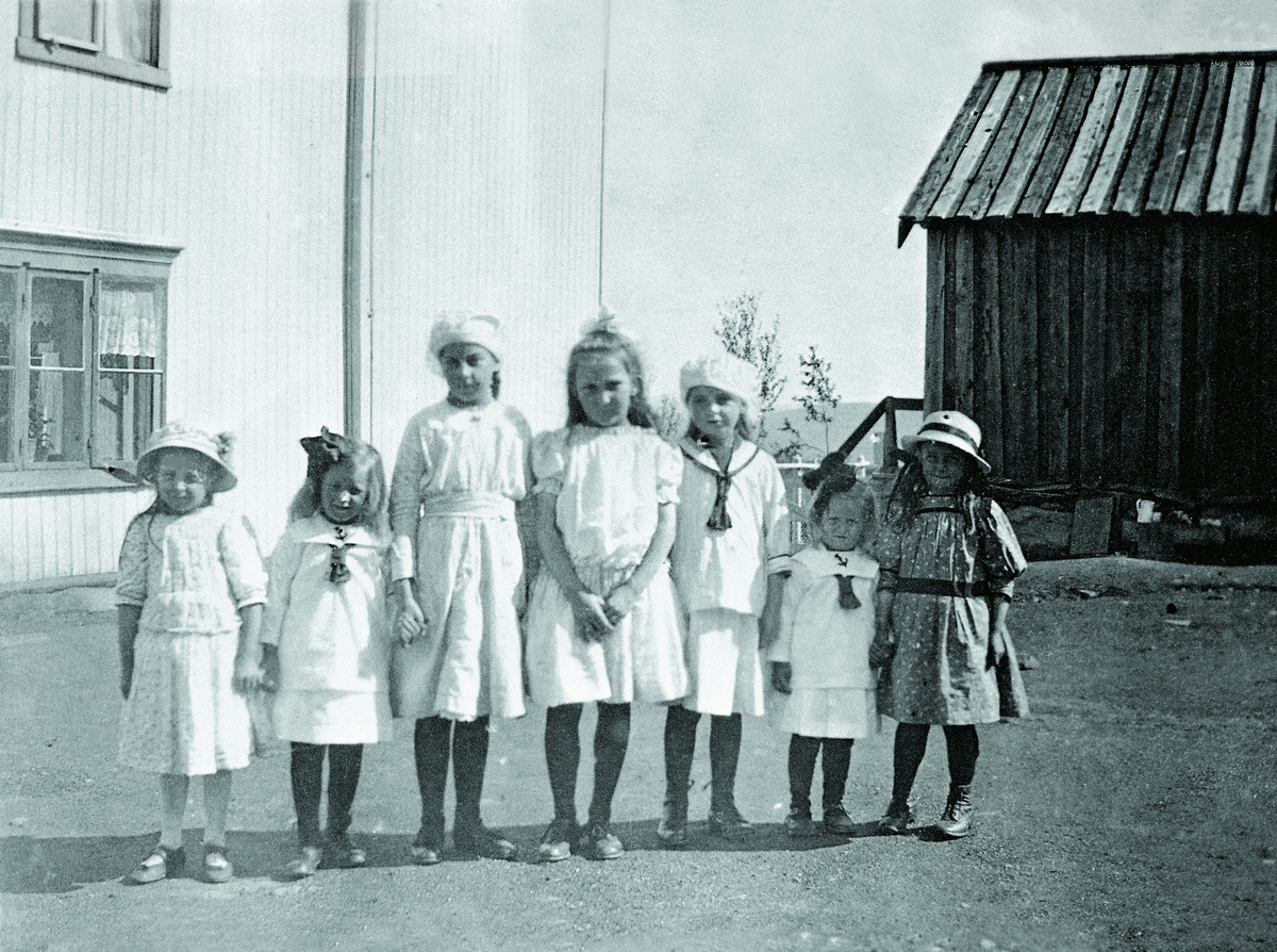 Sju søndagspyntete jenter utafor ingeniørboligen på Kongens gruve, ca 1918