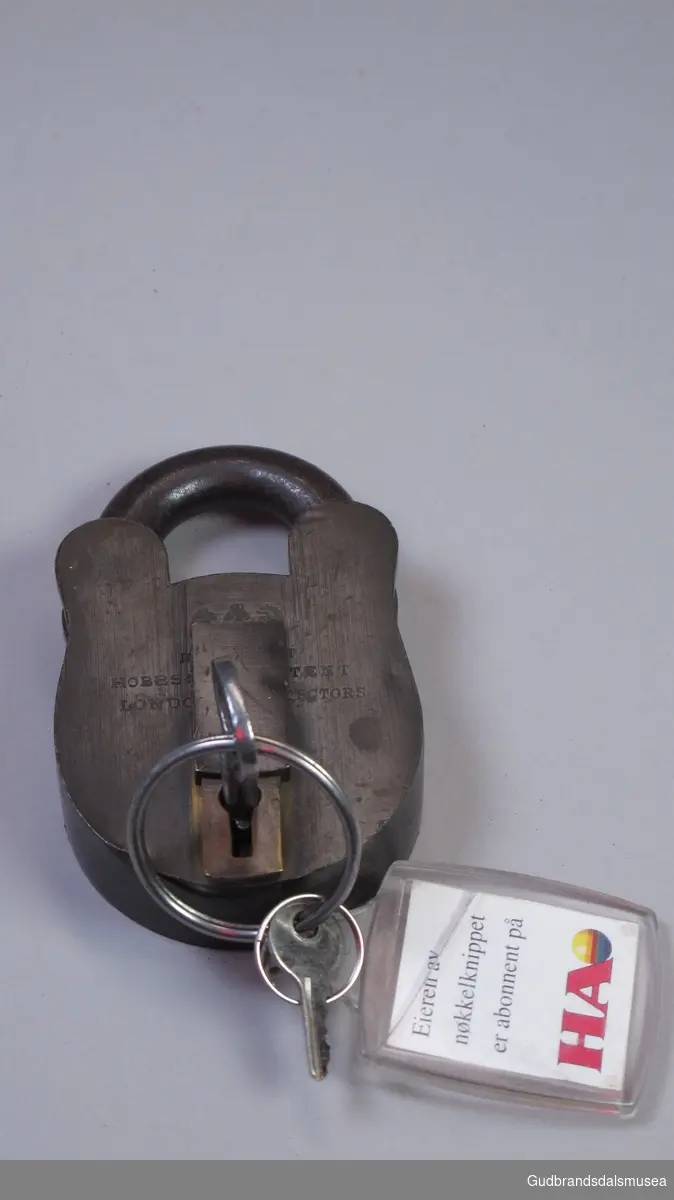 Hengelås  med nøkkel. Produsert i London.   På nøkkelringen  er det også en mindre nøkkel. Nøkkelhullet kan dekkes med et skjold.
