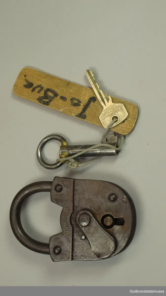 Lås  - hengelås. Produsert i tyskland. Har nøkkel . Også en trioving -nøkkel på samme nøkkelspildre. Nøkkelhullet kan tildekkes med et skjold.