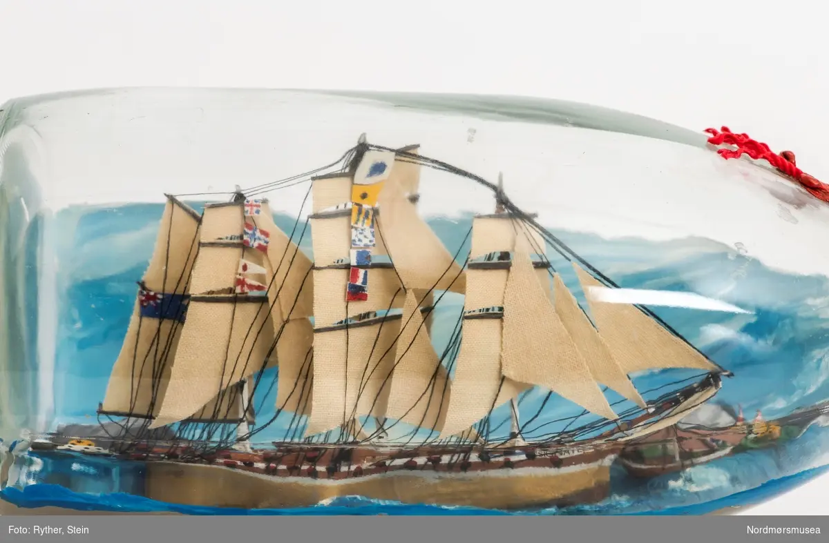 Flaskeskute med modell av HMS Signate (Cygnet). Korken holdes på plass av korknetting fra Martini. Pyntet med silkebånd og tau.