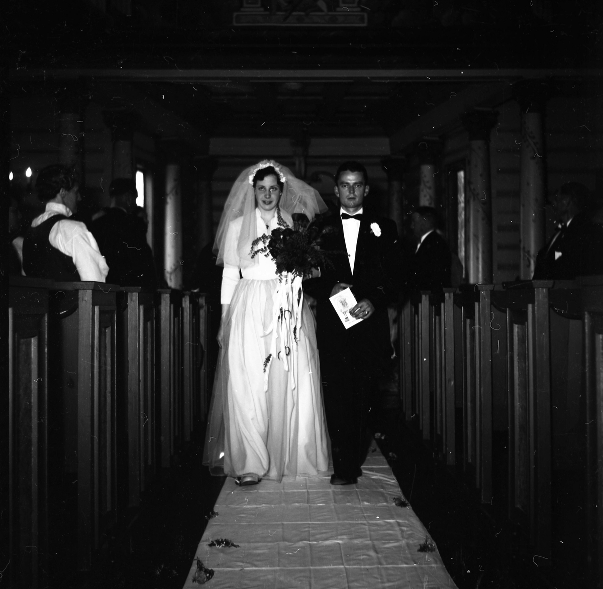 Brudepar i helfigur gående ned kirkegulvet på vei ut etter endt vielse