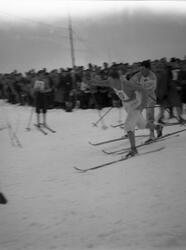 To skiløpere slåss om plassen i løypa. Mange tilskuere sees 