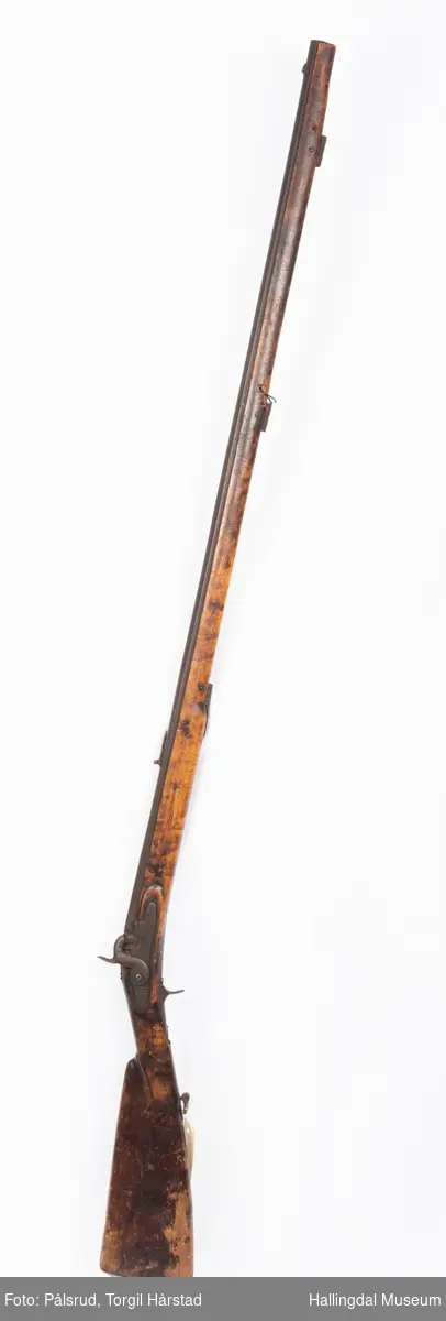 Gevær med perkusjonslås og kassepipe. Kan ha vært ombygd fra flintlås. 
Fra låsen til siktet midt på løpet er løpet kasseformet og har en dekorert overgang til et svakt avrundet åttekantet løp. Det fremste siktet er av messing. Kolbekappen er festet med to skruer. Mangler avtrekksbøyle, reim og ladestokk.