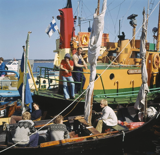 Tävlingsbåtarna ligger i hamnen i väntan på start. Ett gäng unga
killar utgör besättningen på den närmaste båten.