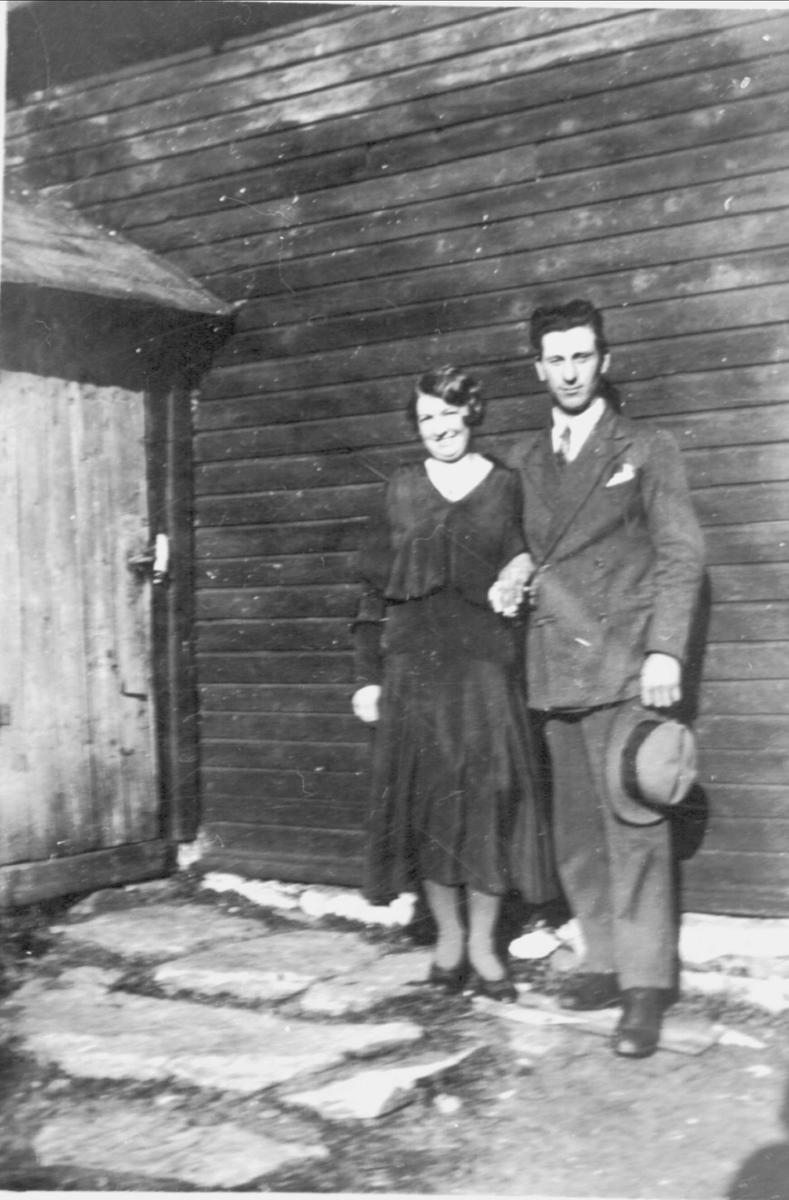Amatørportrett av kvinne og mann stående ved husvegg.