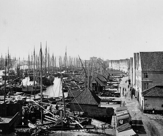 Bildet viser et yrende liv på Bryggen i Bergen i 1860-årene, med tett-i-tett med båter på byfjorden like utenfor Finnegården.