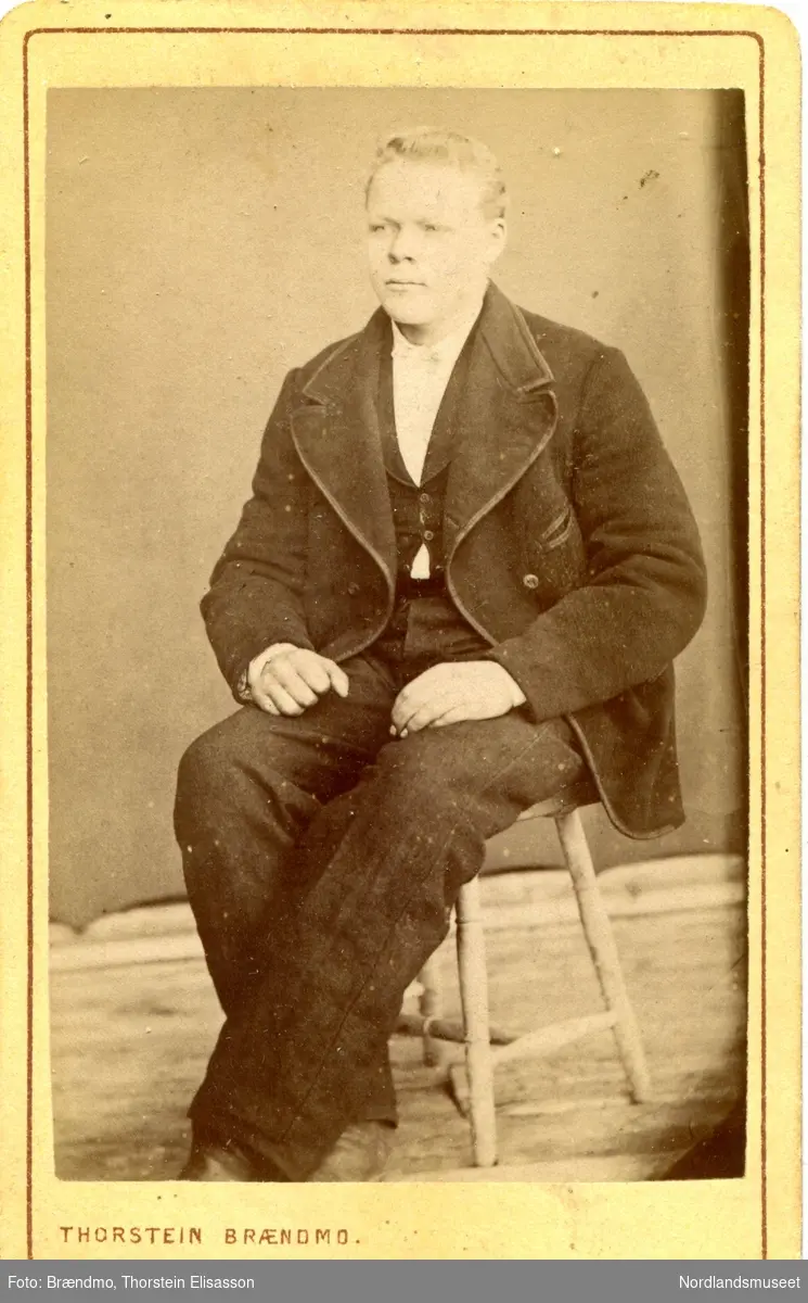 Portrettbilde av en ung mann sittende på en krakk. Nikolai Grønbech.