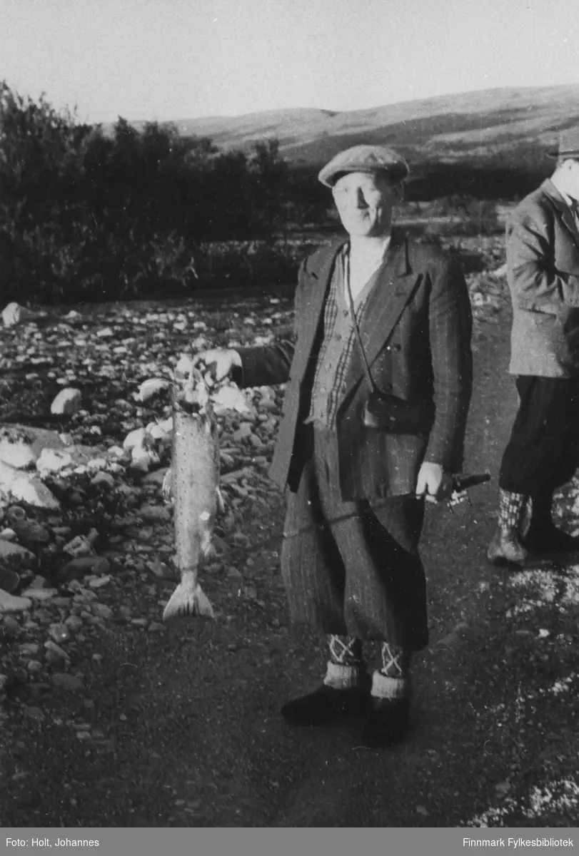 Urmaker Pedersen fra Honningsvåg til venstre har fått en fisk uvist om det er laks eller ørret. Johannes Holt til høyre.
